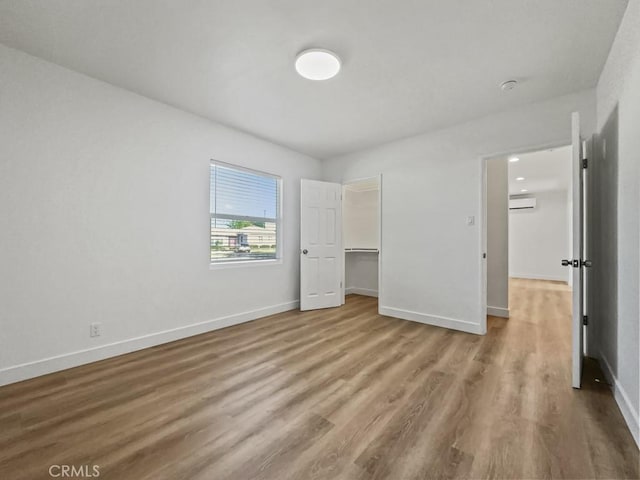 unfurnished bedroom featuring baseboards, wood finished floors, and a wall mounted air conditioner