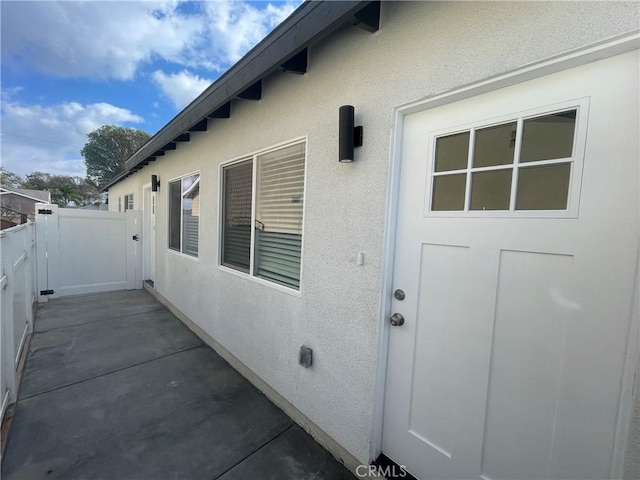 entrance to property with a patio area, fence, a gate, and stucco siding