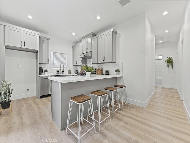 kitchen with under cabinet range hood, a sink, visible vents, gray cabinets, and dishwasher