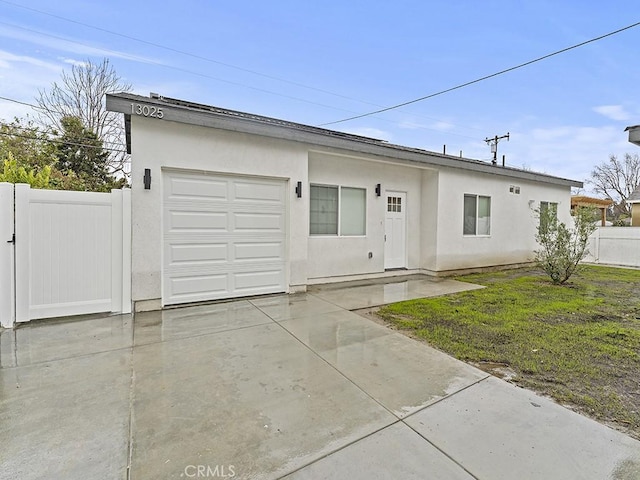 ranch-style home with a garage, concrete driveway, fence, a front lawn, and stucco siding