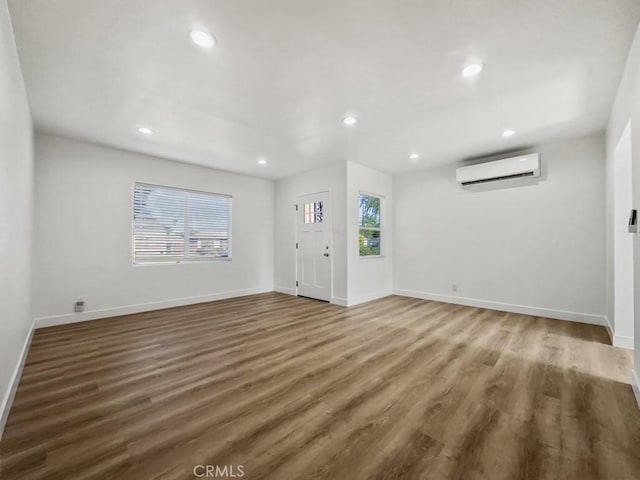 unfurnished living room with recessed lighting, a wall unit AC, baseboards, and wood finished floors