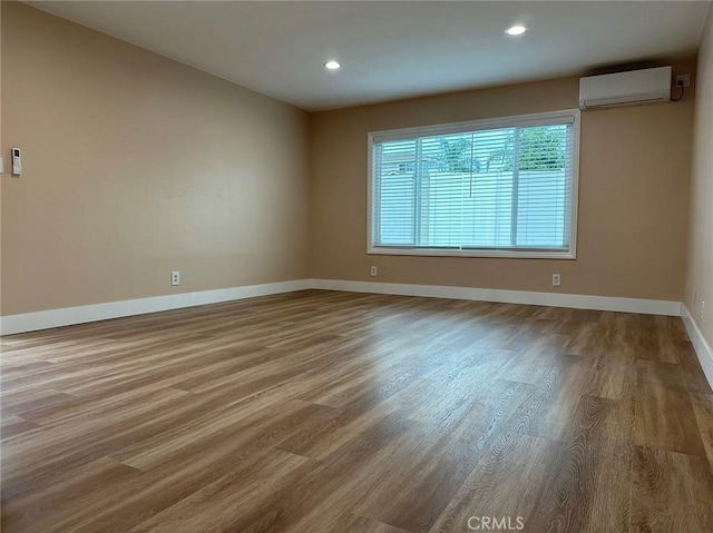 unfurnished room featuring an AC wall unit, recessed lighting, wood finished floors, and baseboards