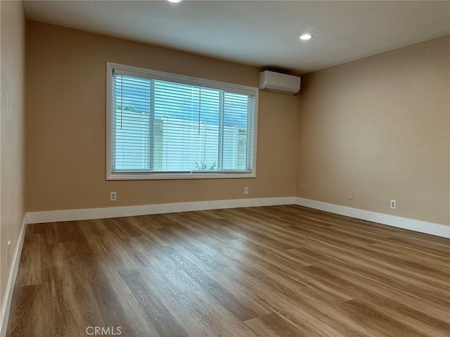 spare room featuring an AC wall unit, recessed lighting, wood finished floors, and baseboards