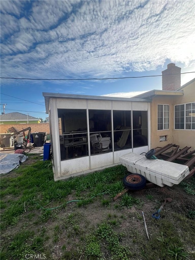 back of house featuring a sunroom, a chimney, and stucco siding