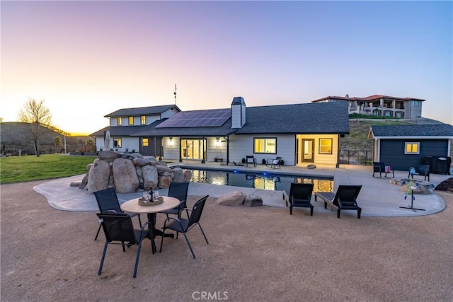 back of property featuring an outbuilding, a patio, roof mounted solar panels, an outdoor pool, and a chimney