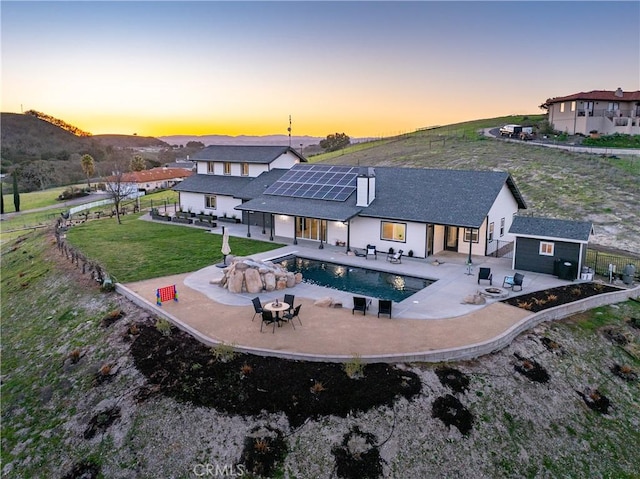 back of house at dusk with a patio area, a yard, an outdoor structure, and fence