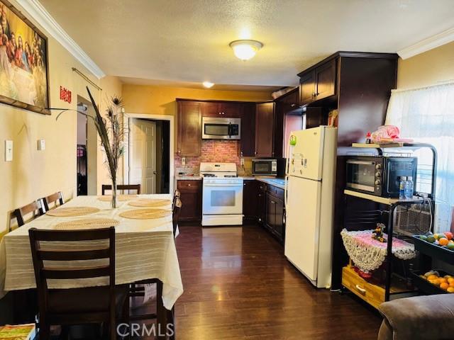 kitchen featuring white appliances, dark brown cabinets, tasteful backsplash, dark wood finished floors, and crown molding