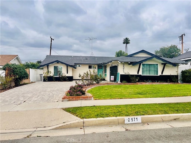 view of front of house featuring decorative driveway, fence, a front lawn, and stucco siding