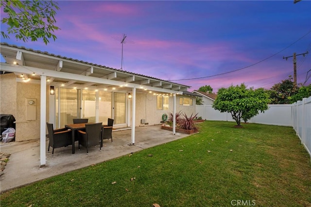 back of house at dusk featuring a lawn, a fenced backyard, stucco siding, and a patio