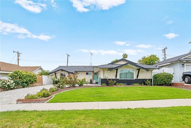view of front facade with decorative driveway, brick siding, fence, a front lawn, and stucco siding