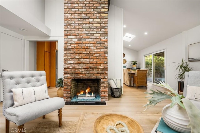 living area with wood finished floors, high vaulted ceiling, a skylight, recessed lighting, and a fireplace