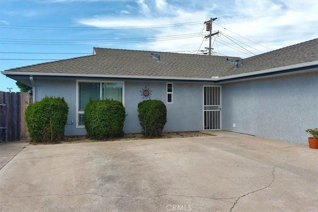 rear view of property with a shingled roof, fence, and stucco siding