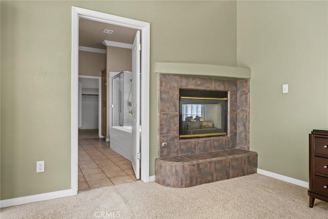 unfurnished living room featuring baseboards, a tiled fireplace, ornamental molding, tile patterned flooring, and carpet floors