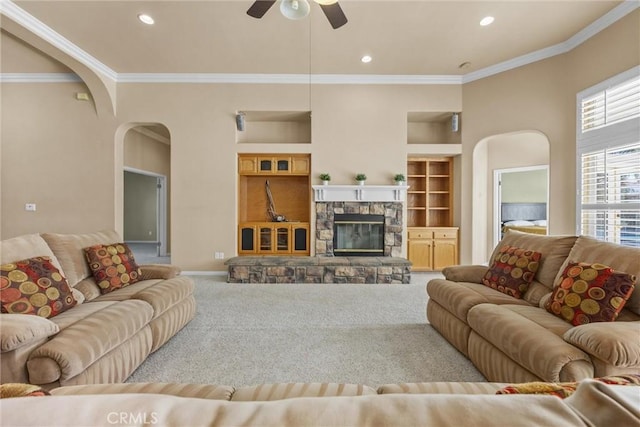 living room featuring arched walkways, ornamental molding, carpet, a stone fireplace, and recessed lighting