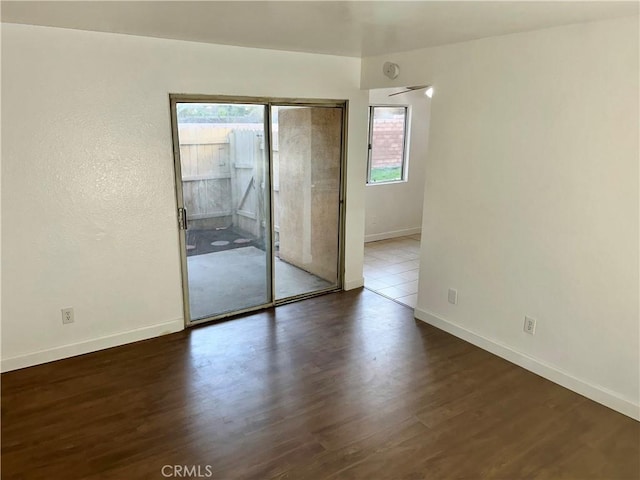 unfurnished room with dark wood-style floors, a wealth of natural light, and baseboards