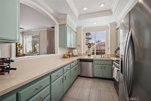 kitchen featuring a tray ceiling, stainless steel appliances, light countertops, a sink, and green cabinetry