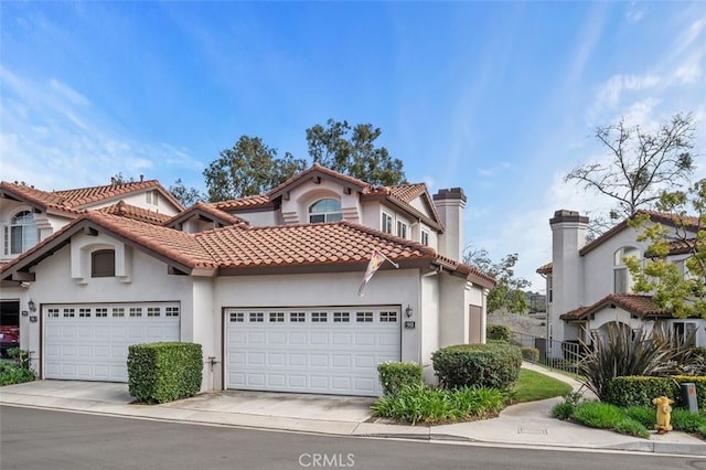 mediterranean / spanish home with a garage, driveway, a tiled roof, and stucco siding