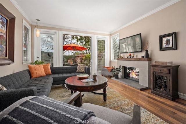 living room with baseboards, a tiled fireplace, wood finished floors, and crown molding