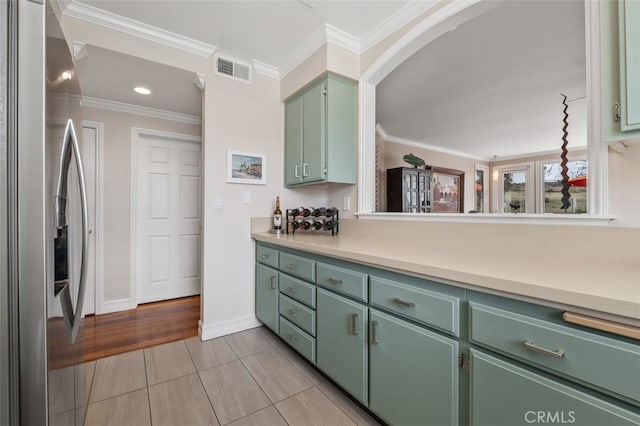 kitchen with visible vents, green cabinets, light countertops, stainless steel refrigerator with ice dispenser, and crown molding