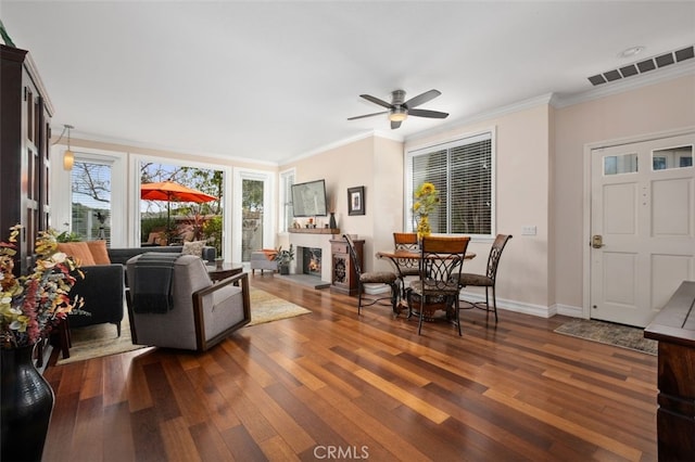 living room with crown molding, visible vents, dark wood finished floors, and a lit fireplace