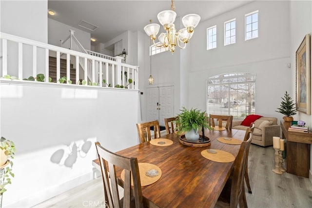 dining area featuring light wood-style floors, a notable chandelier, stairway, and a high ceiling