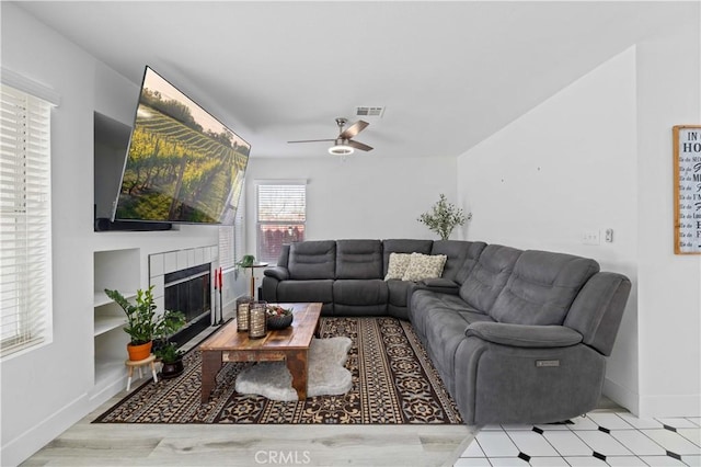 living room with light floors, visible vents, a ceiling fan, a tile fireplace, and baseboards