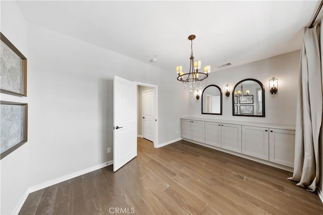 interior space with visible vents, a notable chandelier, baseboards, and wood finished floors