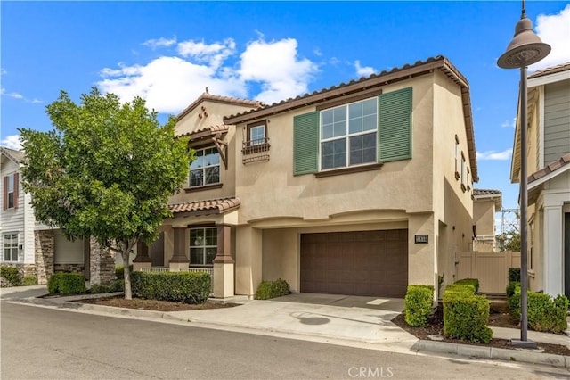 mediterranean / spanish home featuring an attached garage, a tiled roof, concrete driveway, and stucco siding