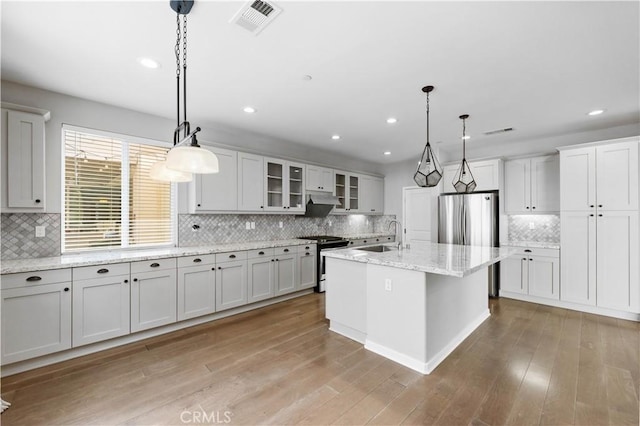 kitchen with under cabinet range hood, light wood-style flooring, glass insert cabinets, and stainless steel appliances