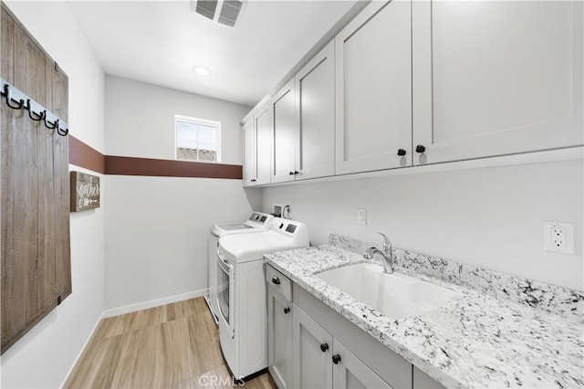 laundry room featuring washing machine and dryer, a sink, visible vents, cabinet space, and light wood finished floors