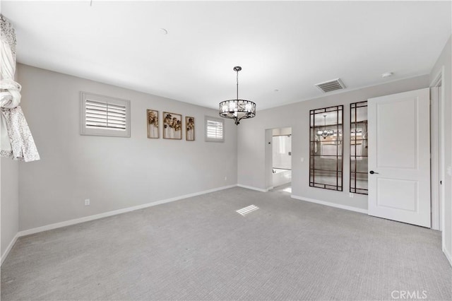 carpeted spare room featuring baseboards, visible vents, and a chandelier