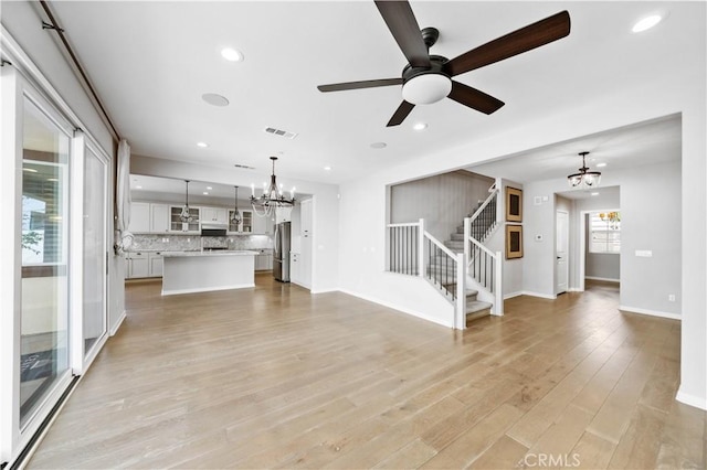 unfurnished living room with light wood-type flooring, visible vents, recessed lighting, and stairs