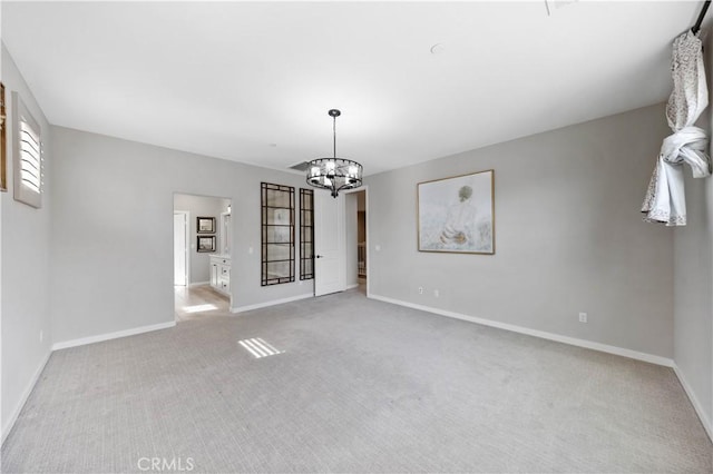 unfurnished room featuring a chandelier, baseboards, and light colored carpet