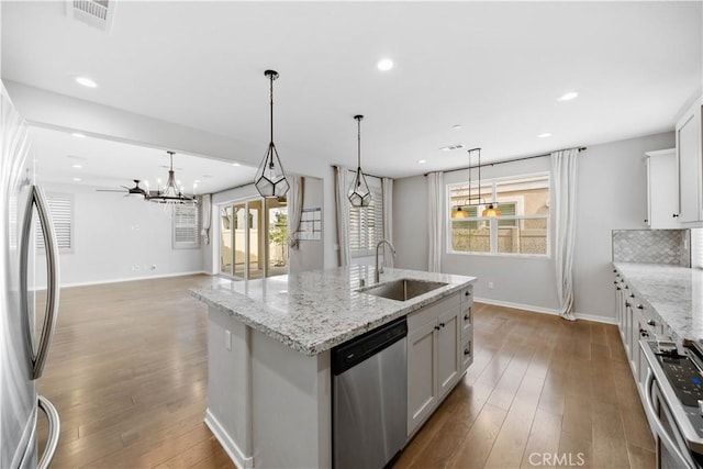 kitchen with a center island with sink, stainless steel appliances, decorative backsplash, a sink, and hardwood / wood-style floors