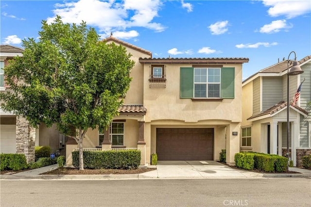 mediterranean / spanish-style home featuring concrete driveway, an attached garage, a tiled roof, and stucco siding