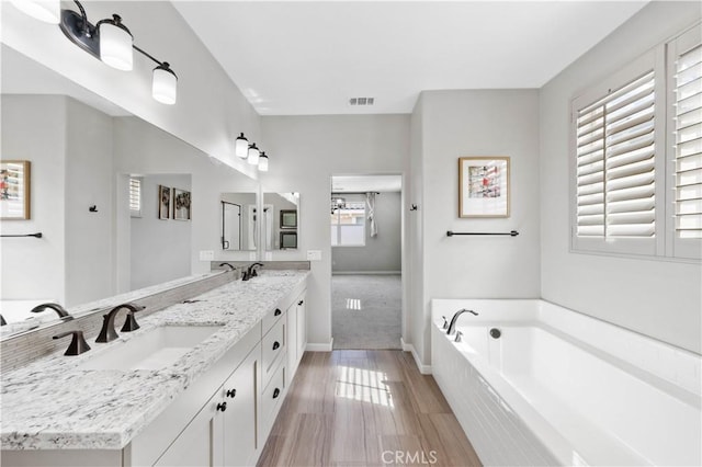 full bath with wood finished floors, visible vents, a sink, and a bath