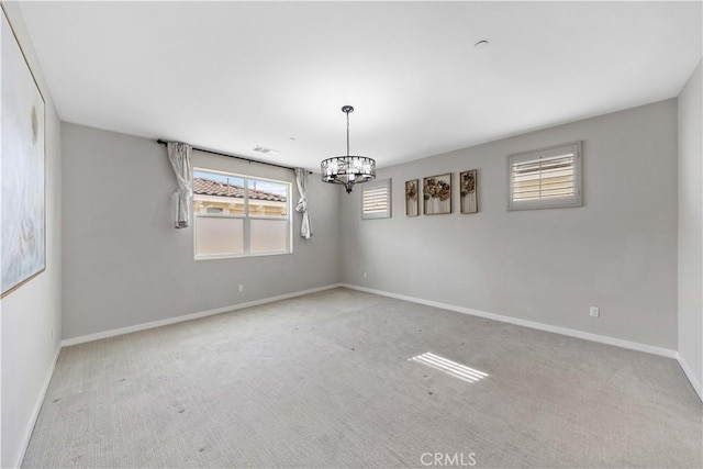 carpeted spare room with an inviting chandelier and baseboards