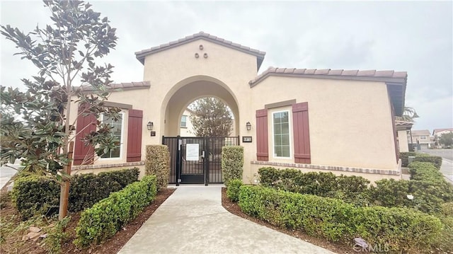 entrance to property featuring a tile roof, a gate, and stucco siding