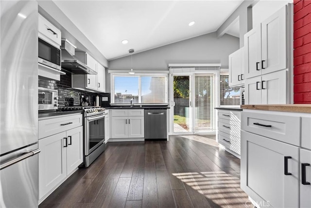 kitchen featuring lofted ceiling with beams, wall chimney range hood, appliances with stainless steel finishes, and dark wood-type flooring