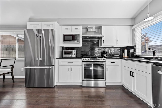 kitchen with dark countertops, wall chimney exhaust hood, dark wood-style flooring, stainless steel appliances, and a sink