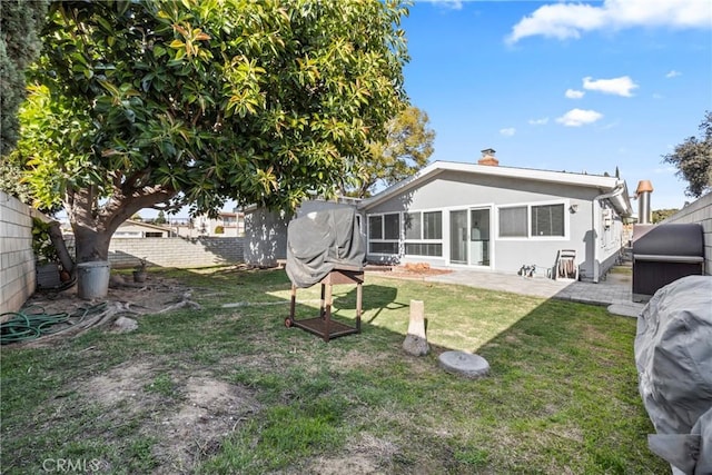 rear view of house featuring a fenced backyard, a chimney, a yard, a patio area, and stucco siding