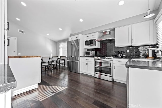 kitchen featuring stainless steel appliances, a sink, white cabinets, wall chimney range hood, and dark countertops