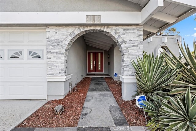 doorway to property with a garage, stone siding, and stucco siding