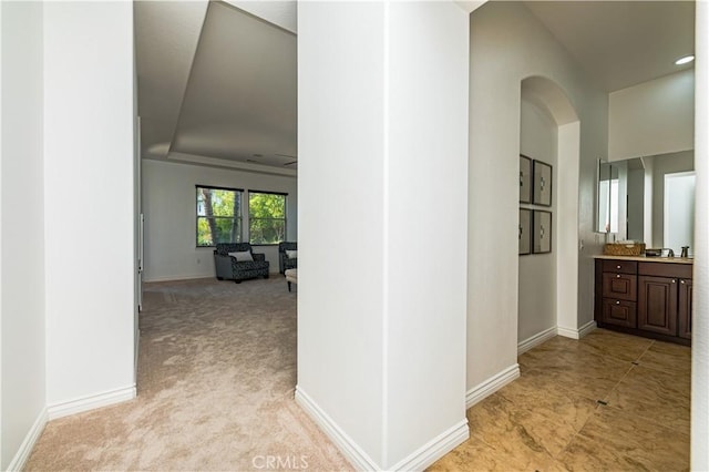 corridor with light carpet, a sink, arched walkways, and baseboards