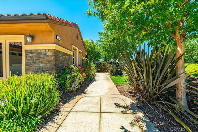 view of property exterior with a garage, a tiled roof, stone siding, and stucco siding