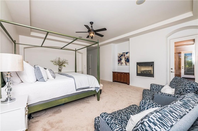 bedroom featuring baseboards, a glass covered fireplace, and light colored carpet