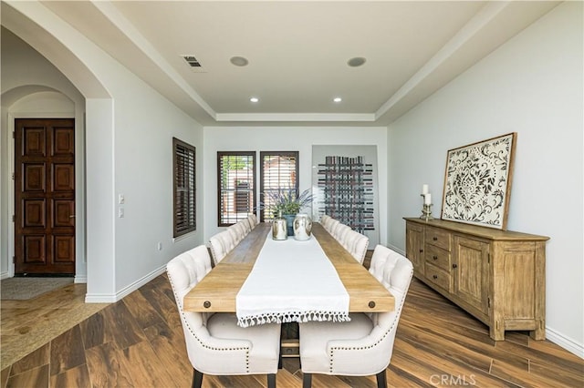 dining area with baseboards, visible vents, arched walkways, a raised ceiling, and dark wood-type flooring