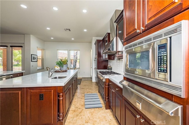 kitchen featuring a warming drawer, tasteful backsplash, stainless steel microwave, a sink, and an island with sink