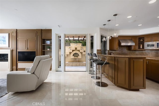 3824 Vista Blanca, San Clemente, CA 92672 - kitchen featuring stainless steel microwave, wall chimney exhaust hood, backsplash, a breakfast bar area, and decorative light fixtures