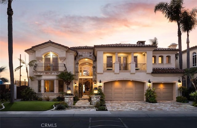 mediterranean / spanish house with a garage, a balcony, a tile roof, decorative driveway, and stucco siding